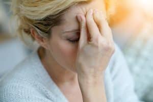 Woman with her eyes closed, holding the front of her forehead with her fingertips. 